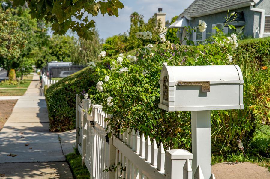 Image of a mailbox on a quiet street with a fence and flowers in the background