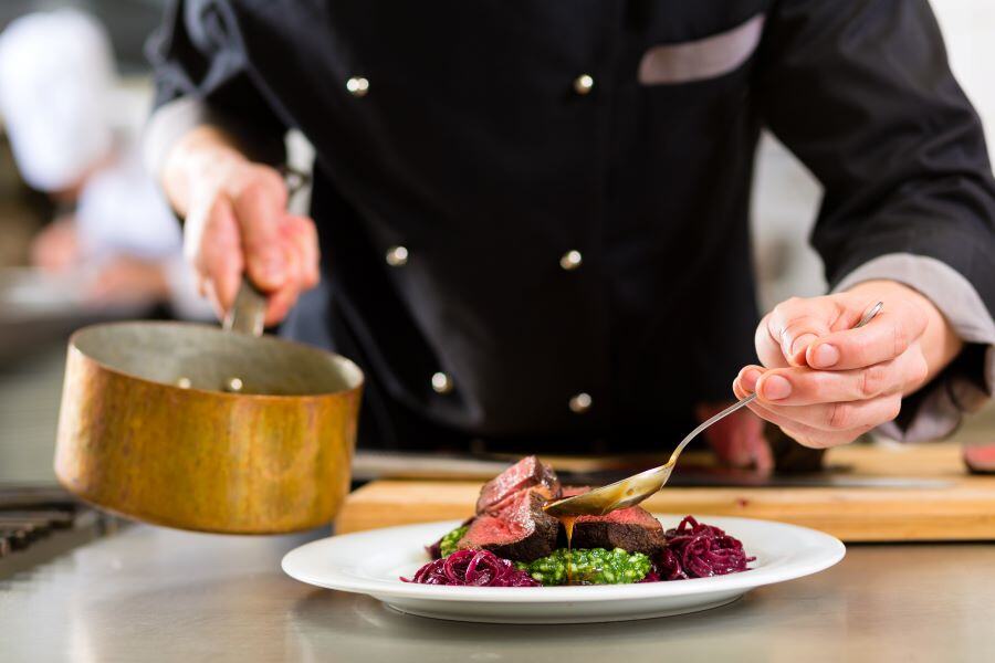 Image of a chef in a restaurant uniform finalizing a plate and meal