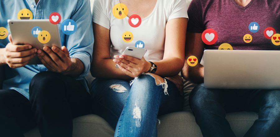 Image of three people sitting on a bench using digital devices with social icons around them